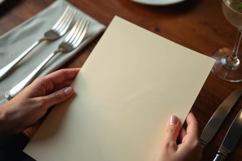 Hand holding blank menu paper on luxury restaurant table.